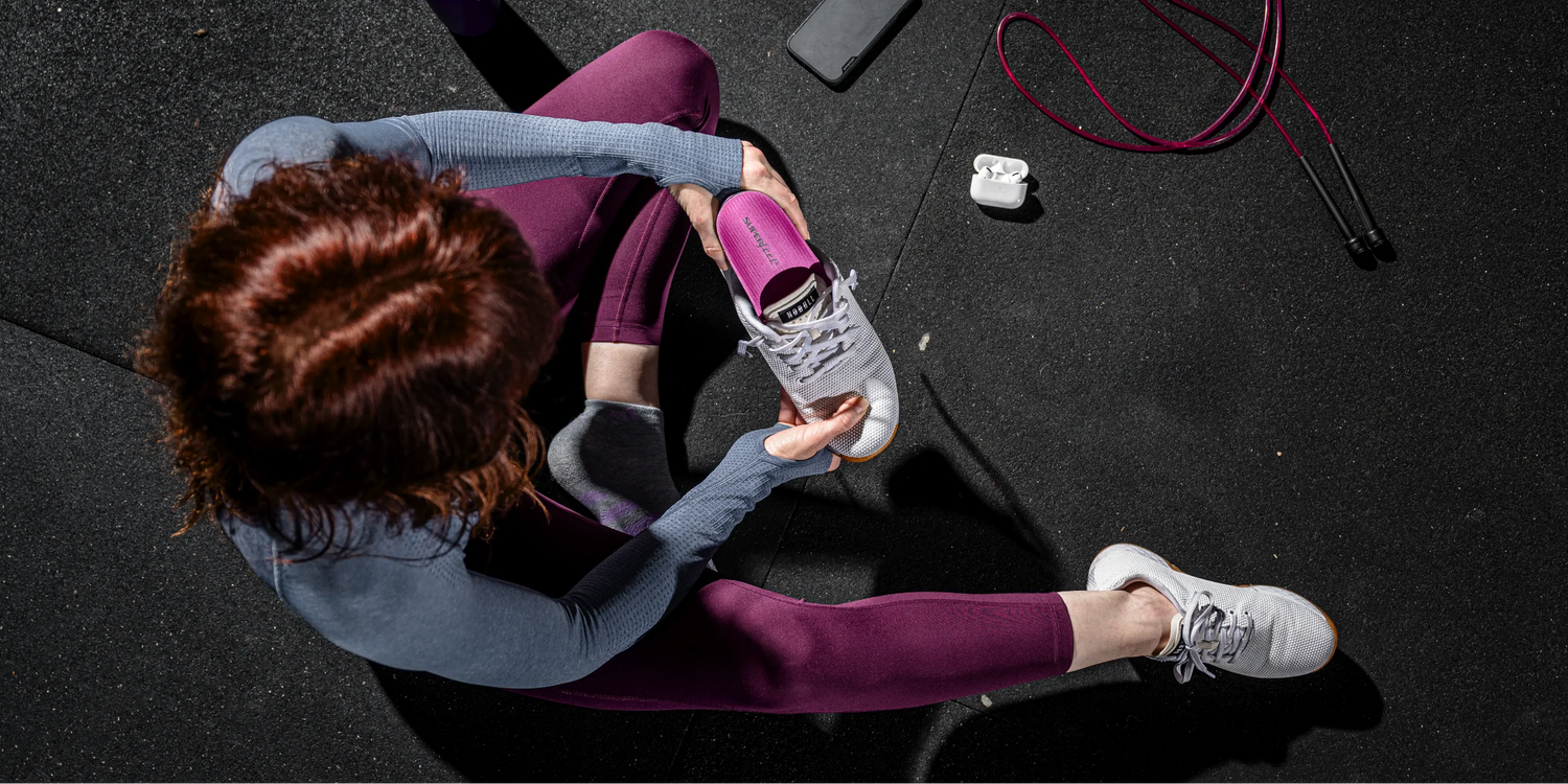 Woman in gym inserting Superfeet insole into gym shoe for workout.