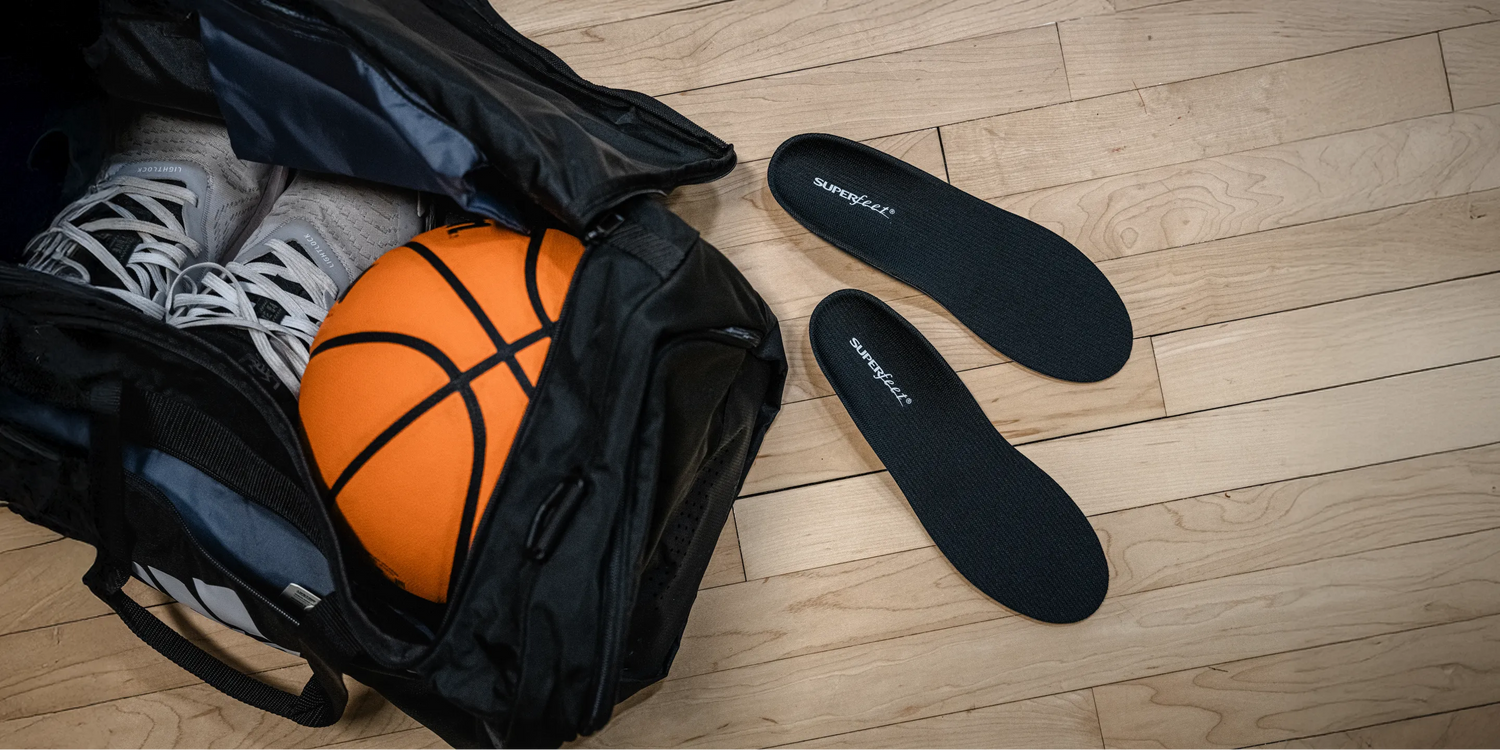 Image of a pair of  Superfeet Support Low Arch insole on ground next to a gym bag with shoes and a basketball inside.