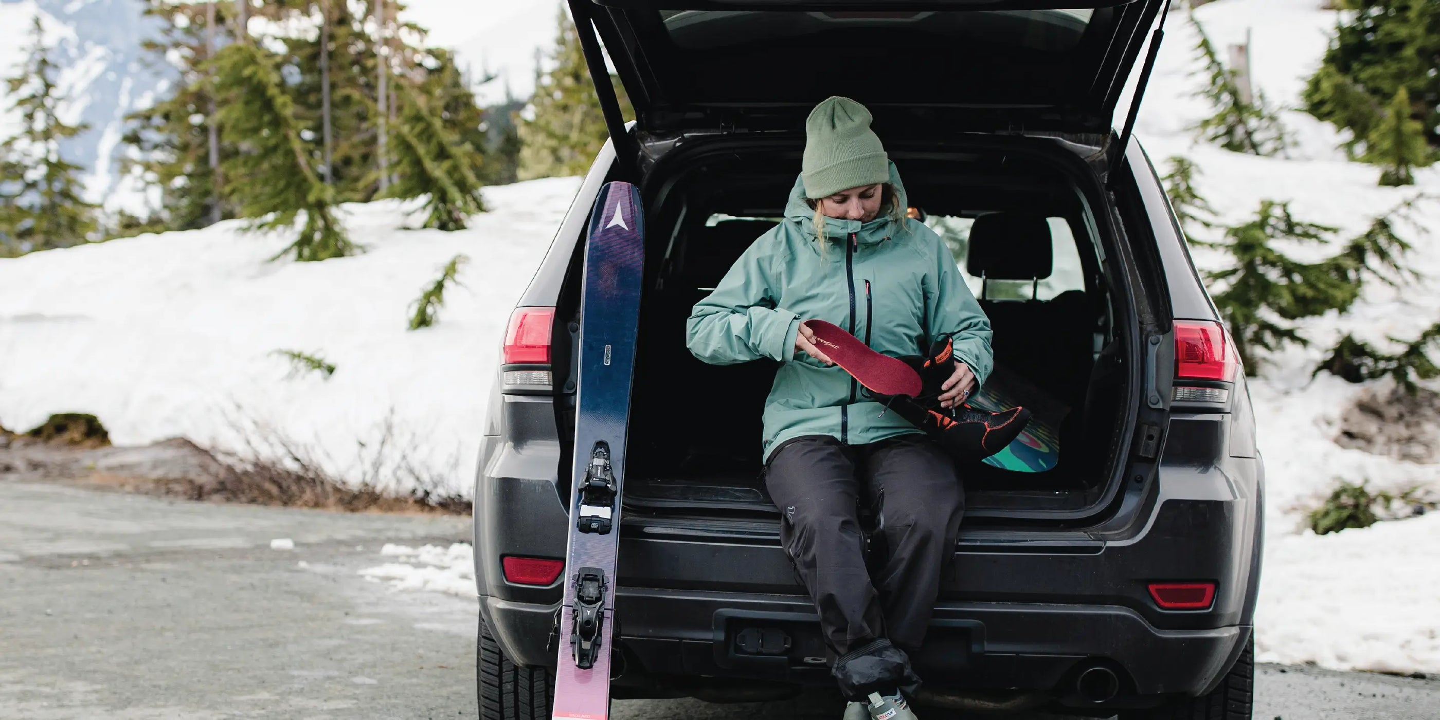 Woman sitting in vehicle in snow gear getting ready to ski and putting a Super Winter Support insole into her ski boot.